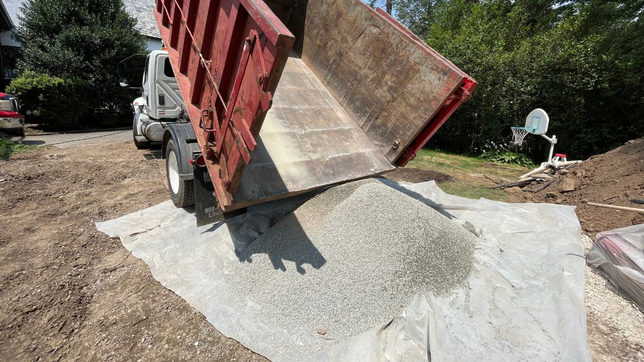 Subbase aggregate installation for permeable pavers with geotextile fabric and dump truck