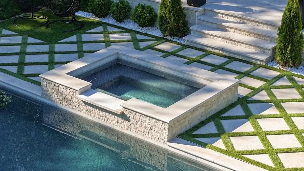 Diagonal grid pattern of stone pavers with grass in between around a modern swimming pool and spa.